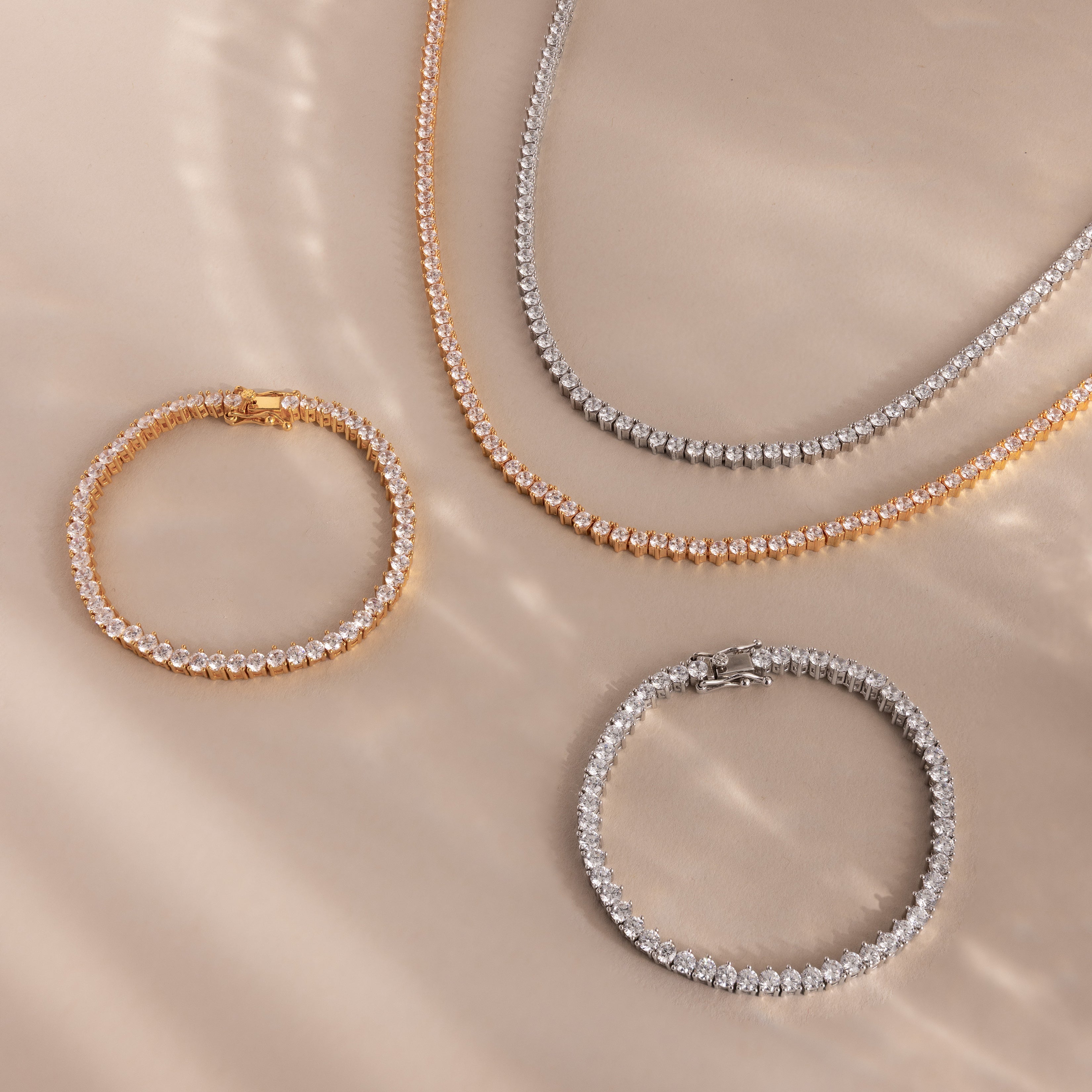 The 3-Prong Diamond Tennis Necklace & Bracelet Set, featuring gold and silver tone pieces with a 3-prong diamond bracelet, is displayed on a beige surface.