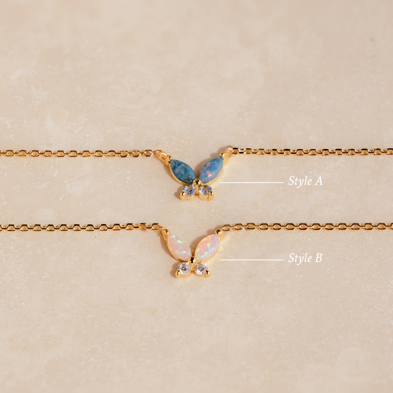 Two gold chain bracelets—one with a blue butterfly charm and one with a white opal charm—rest on beige, perfectly complementing your Opal Butterfly Necklace Set.