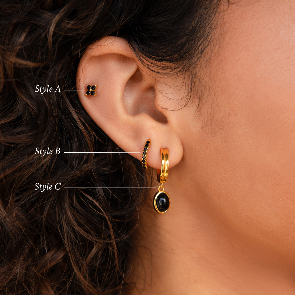 Close-up of a woman's ear with three gold earrings from the Onyx Diamond Earrings Set, featuring elegant details like Black Gemstone Drop Hoops and Black Flower Studs.