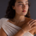 Woman in a white draped top wears the Dainty Diamond Tennis Necklace & Bracelet Set in White Gold, looking thoughtfully to the side.