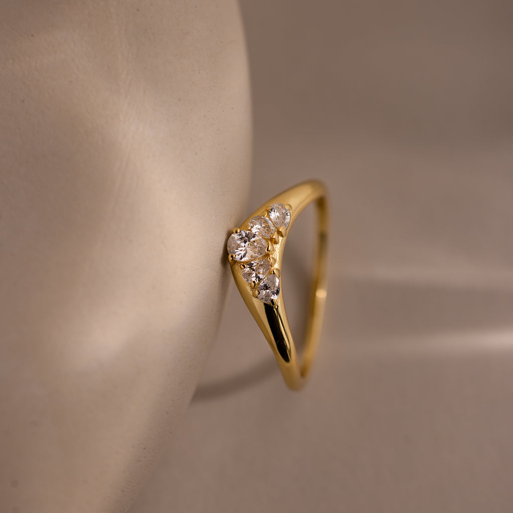 Close up of a gold curve ring featuring five pear diamonds resting vertically against a neutral prop.