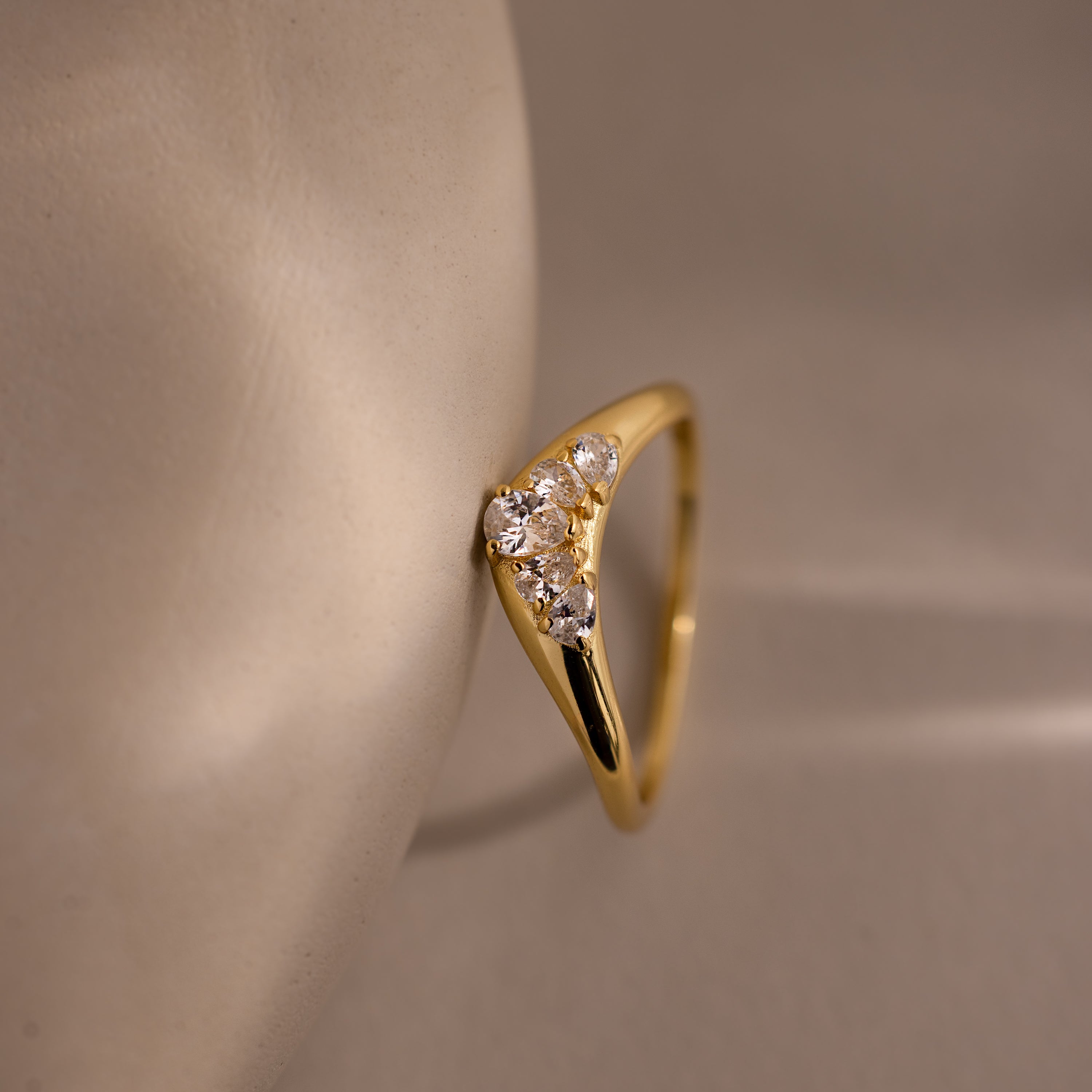 Close up of a gold curve ring featuring five pear diamonds resting vertically against a neutral prop.
