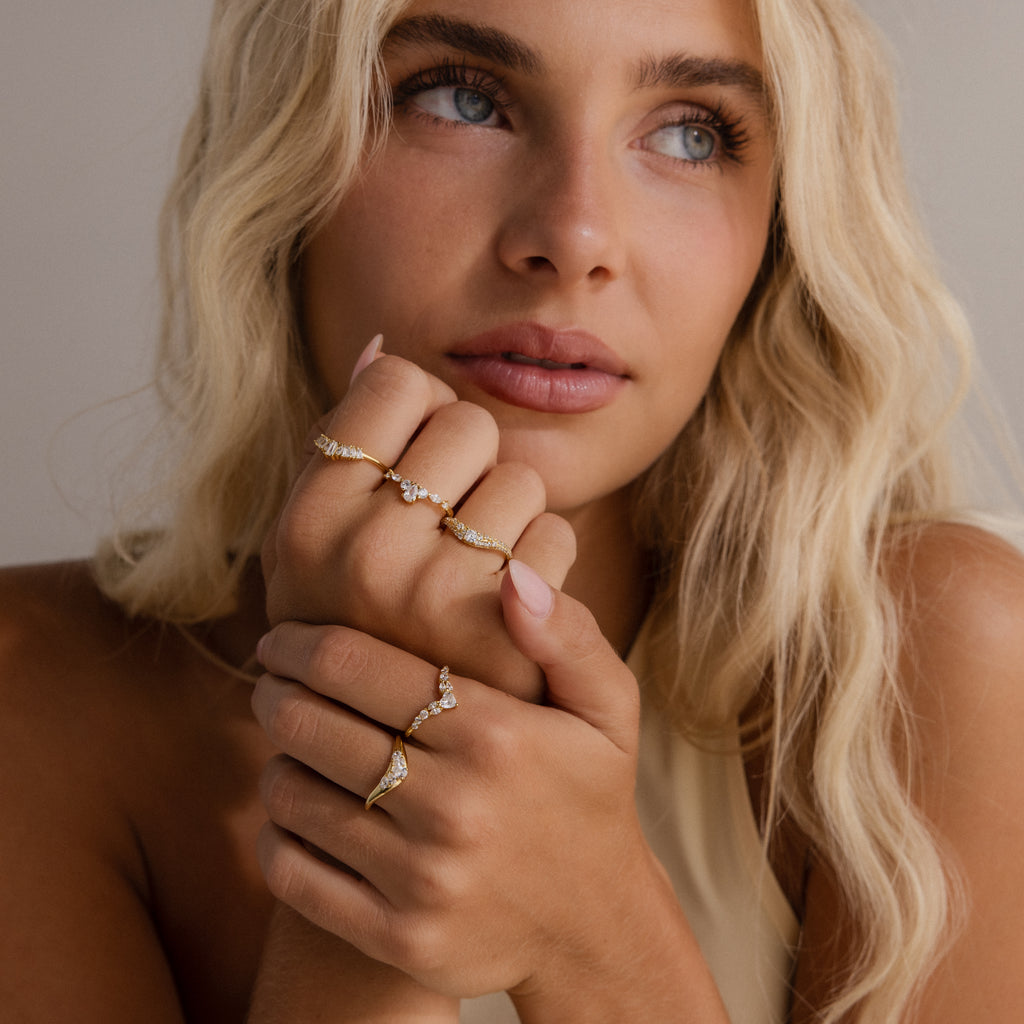 Model wearing multiple gold diamond rings with curved bands, featuring clusters of round and pear cut stones.