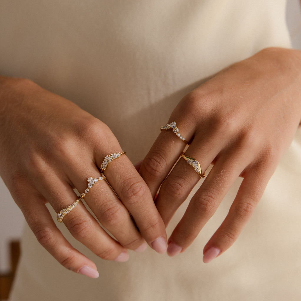 Model wearing multiple gold rings featuring clusters of round and pear shaped diamonds in unique curved band designs.