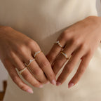 Model wearing multiple gold rings featuring clusters of round and pear shaped diamonds in unique curved band designs.