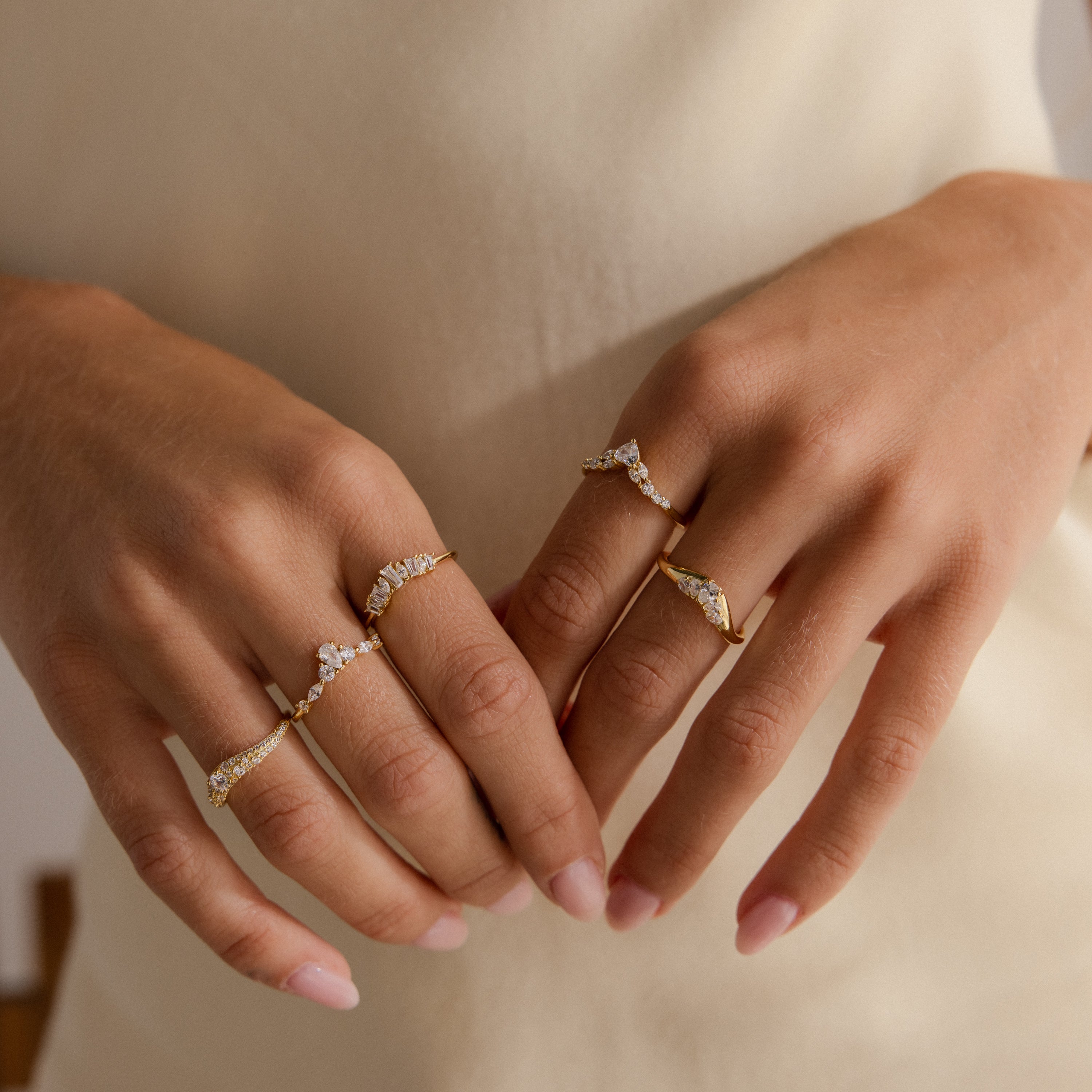 Model wearing multiple gold rings featuring clusters of round and pear shaped diamonds in unique curved band designs.