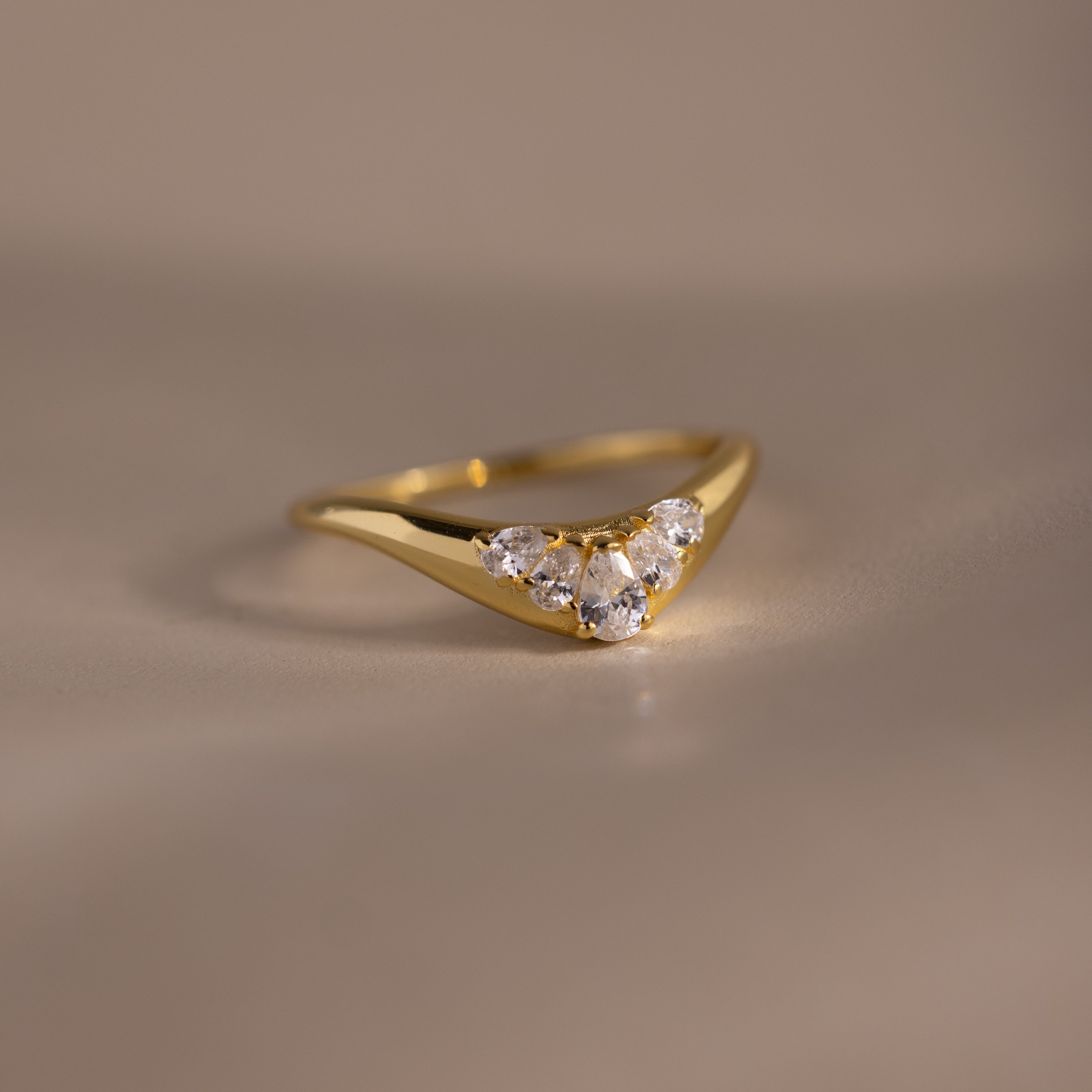 Gold curve ring with five pear cut diamonds set in a V shaped design, displayed on a neutral background.