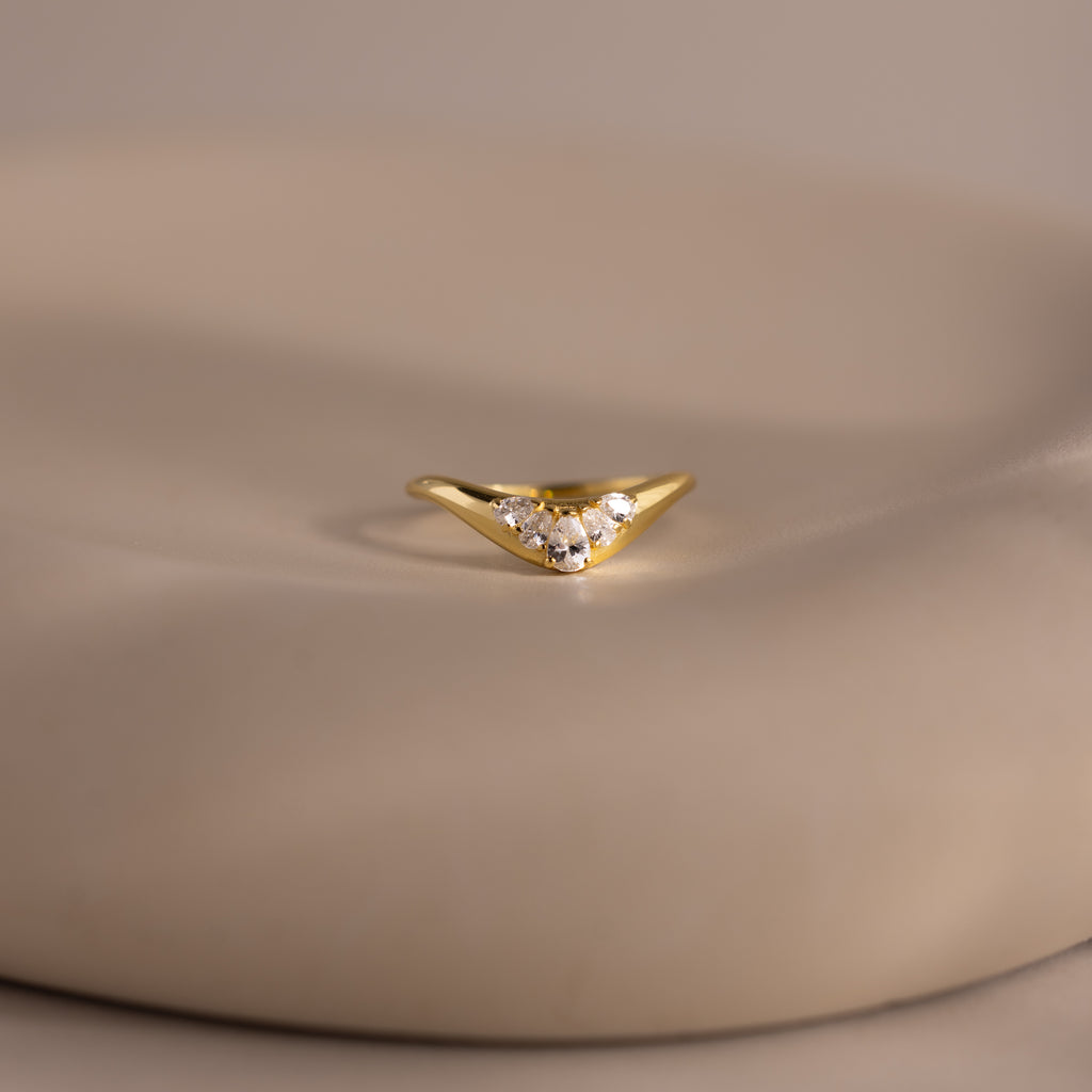 Gold curve ring with five pear cut diamonds in a graduated V shaped setting, displayed on a smooth neutral surface.