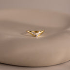 Gold curve ring with five pear cut diamonds in a graduated V shaped setting, displayed on a smooth neutral surface.