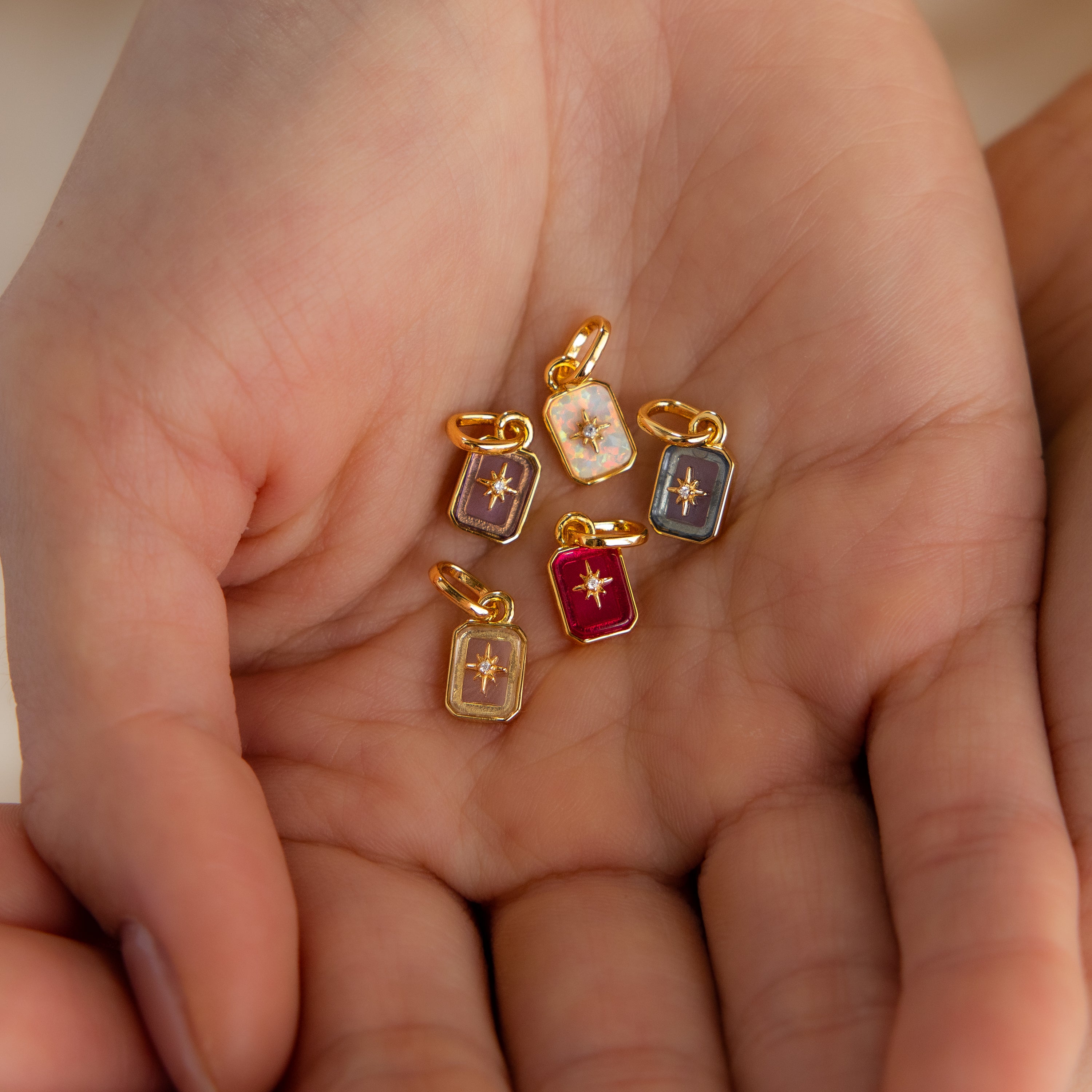 Multiple gold north star birthstone charms in hand.