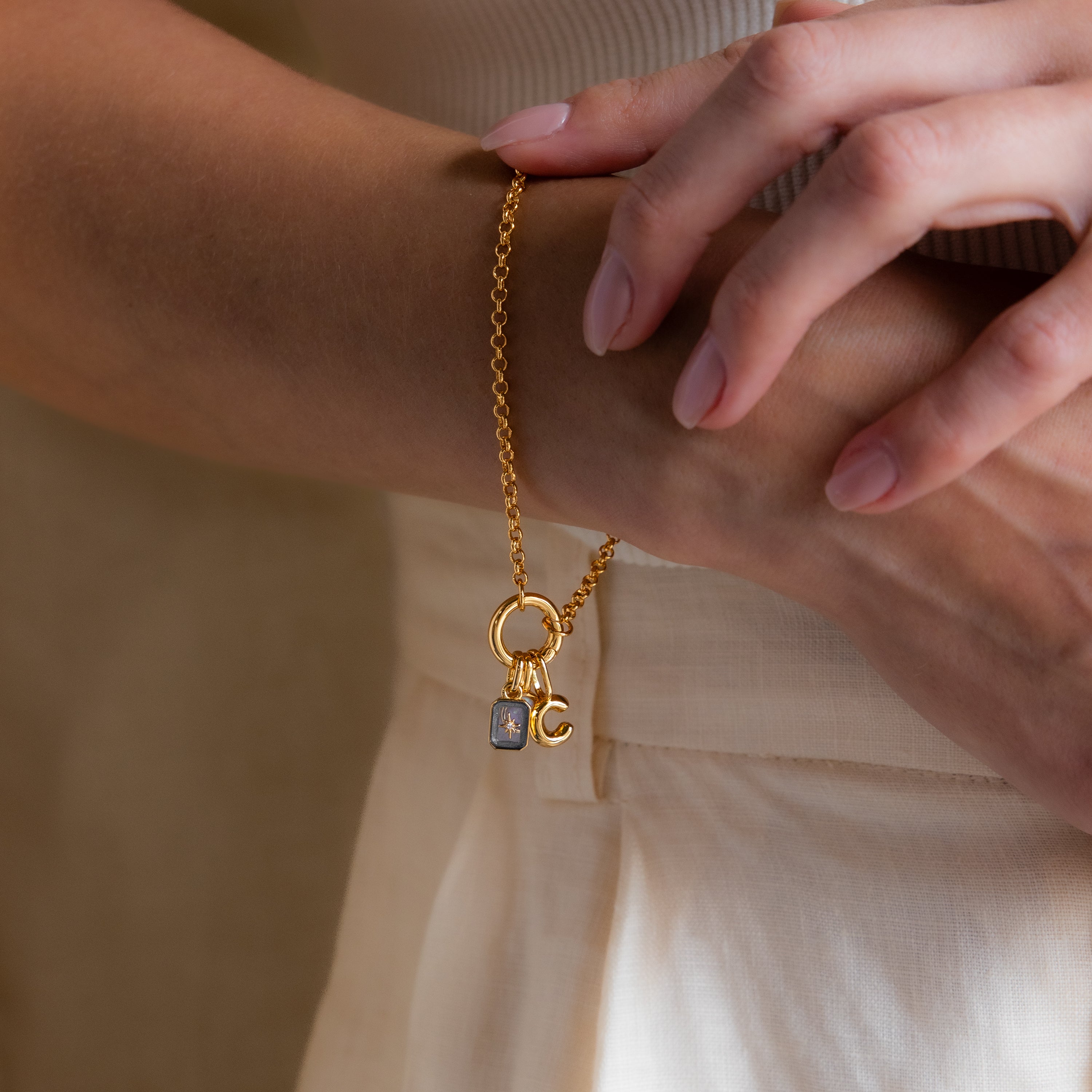 Model wearing a dainty gold rolo charm bracelet with an opal signet charm, bubble letter "C" charm, and aquamarine north star charm.