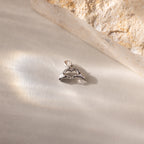 A close up of a silver Heart Hands charm placed on a light surface beside a stone.