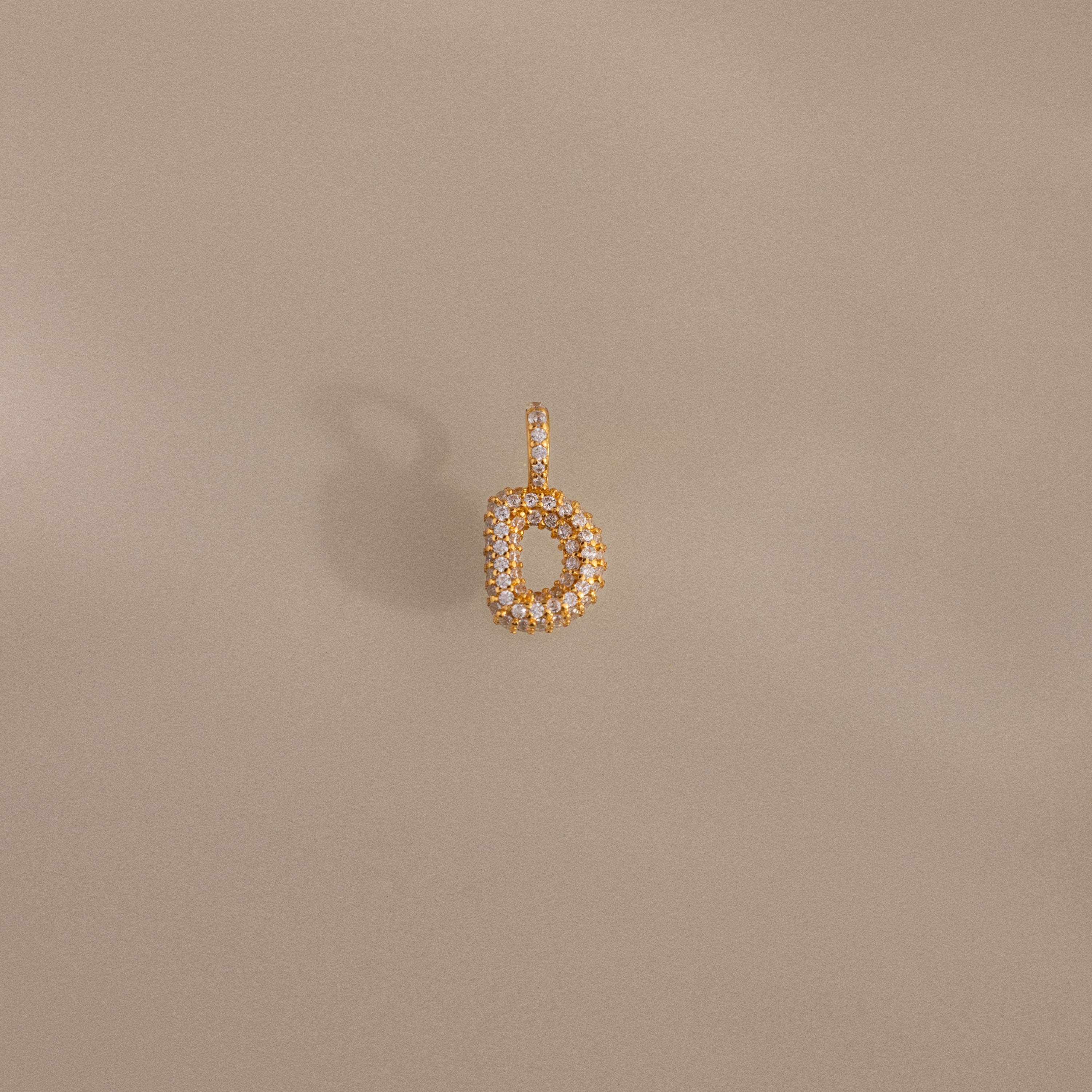 The Pave Bubble Letter Charm is a gold letter "b" pendant adorned with small diamonds, shown against a beige background.