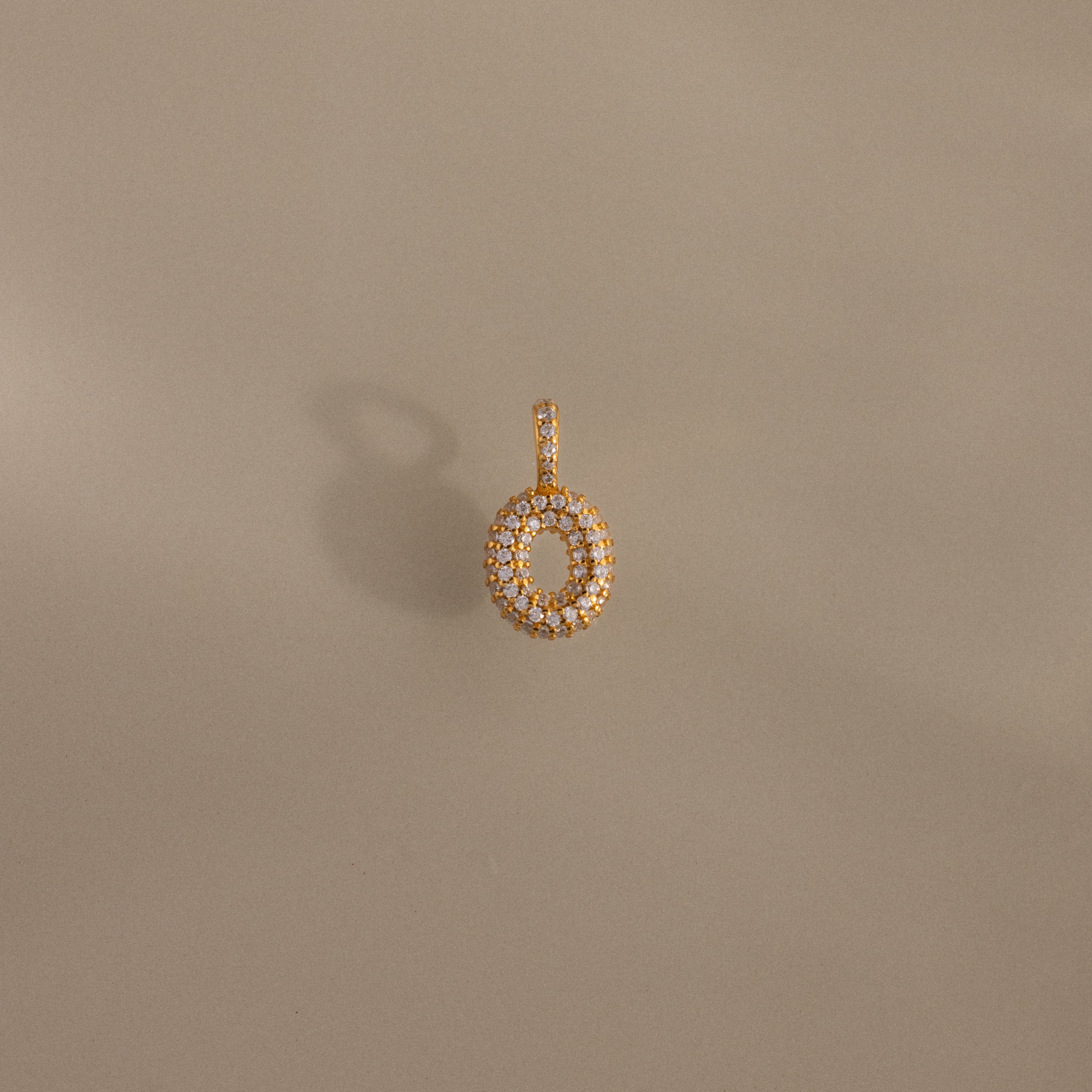 Pave Bubble Letter Charm pendant encrusted with small white stones, shown on a plain beige background.
