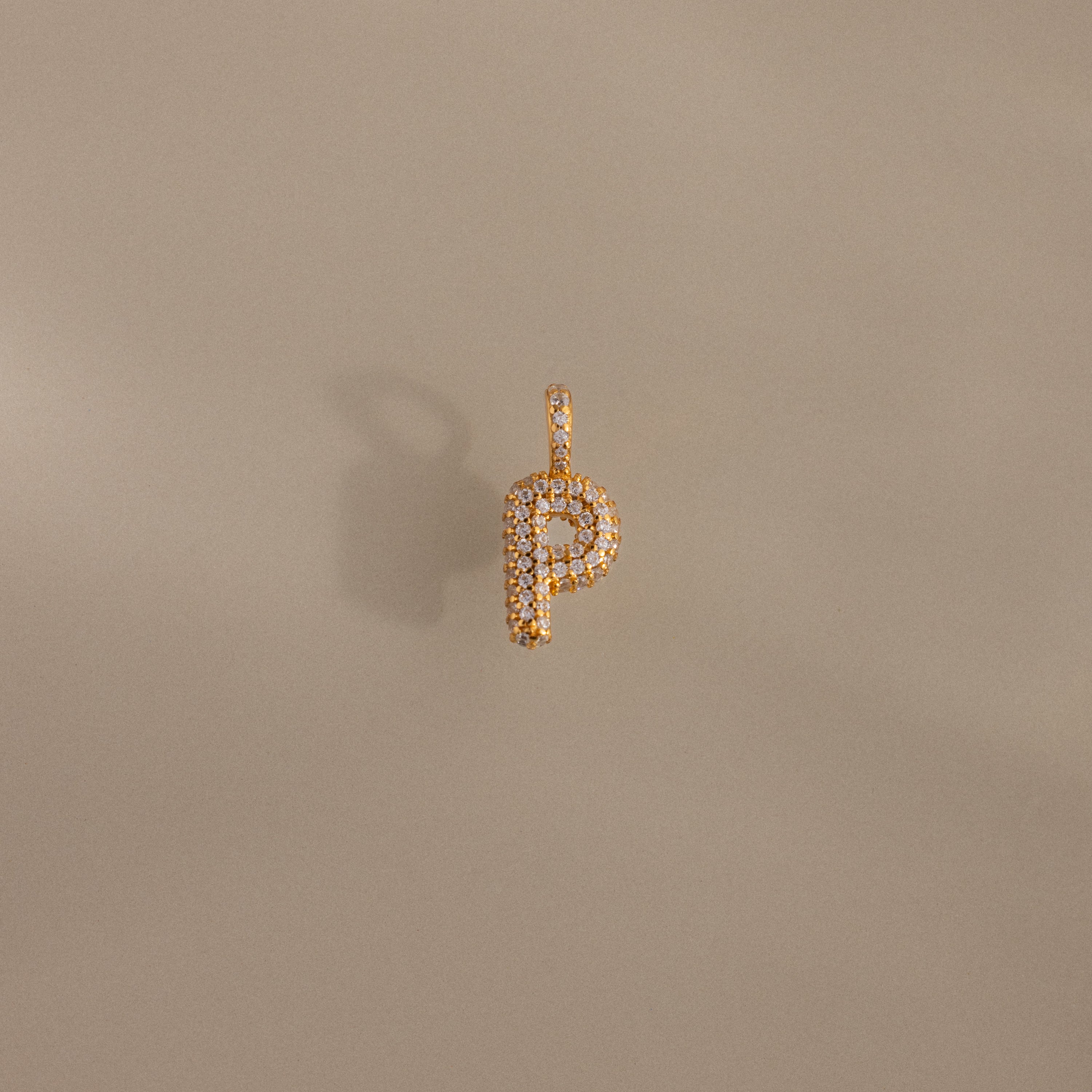 The Pave Bubble Letter Charm is a gold pendant shaped like the letter P, featuring diamond-studded lettering and a sparkling pavé finish, shown on a neutral background.