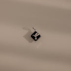 The Onyx Hummingbird Charm in Silver rests on a smooth beige surface with soft shadows—a stylish accessory that brings a unique flair to your jewelry collection.