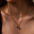 A woman layers two gold necklaces, one featuring the Onyx Honeybee Charm with initial charms, over a chic black top.