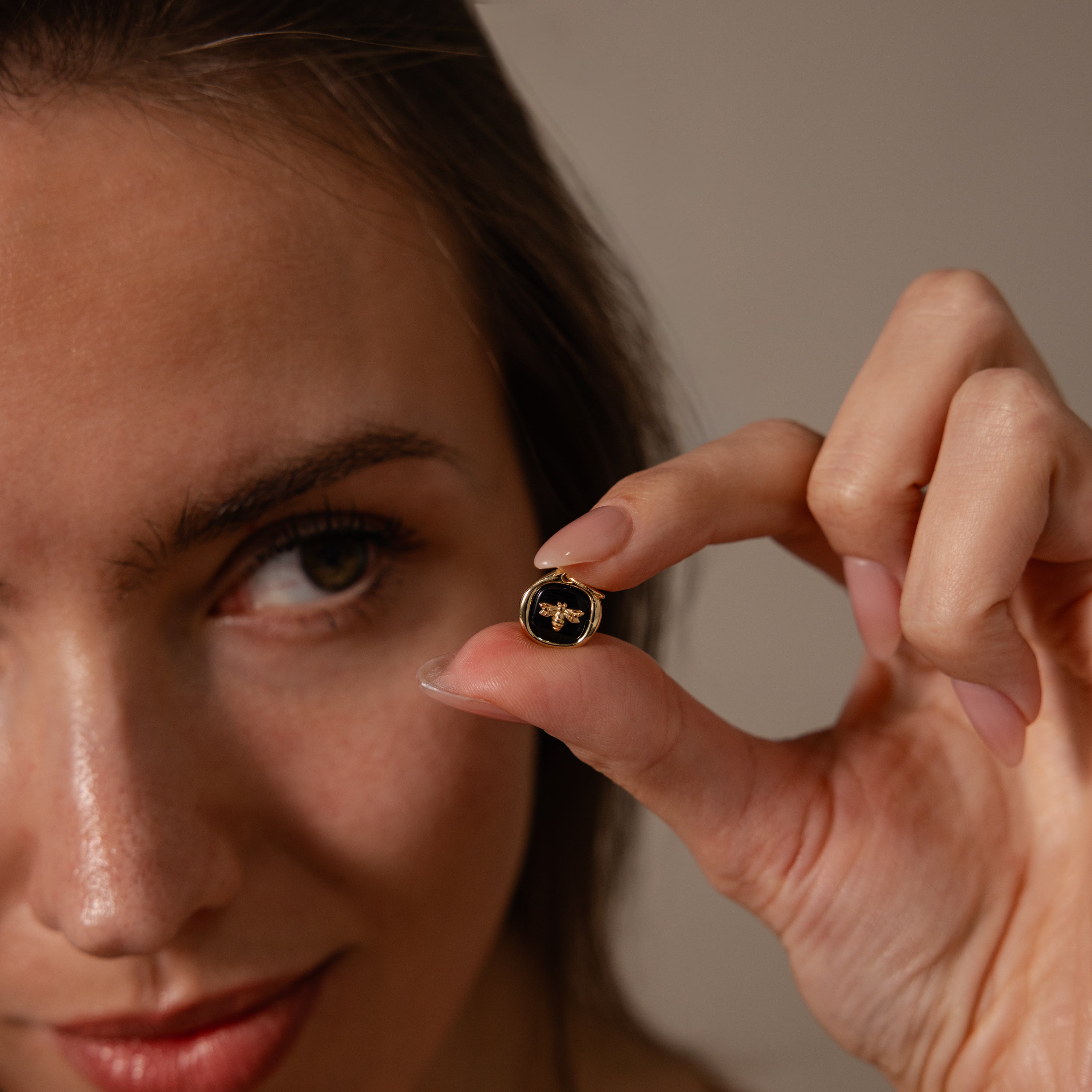 A woman holds the Onyx Honeybee Charm in 18K Gold, a small round pin featuring a gold bee design—please provide the actual product description to identify important SEO keywords.