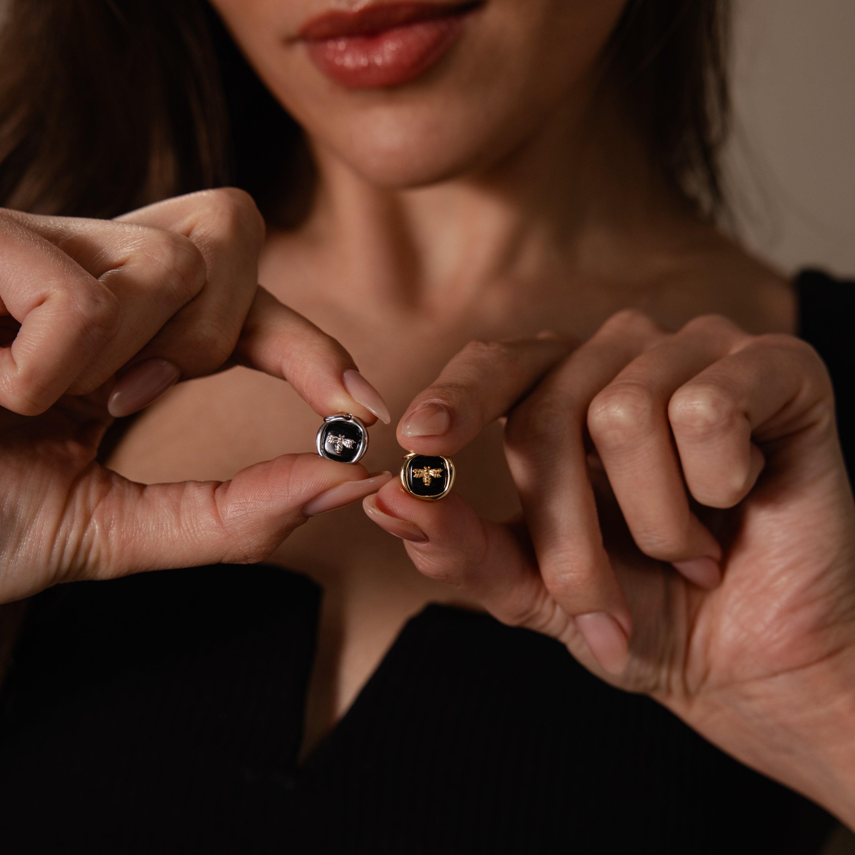 A woman holds the Onyx Honeybee Charm in Silver in front of her chest—this elegant accessory is perfect to elevate your style.