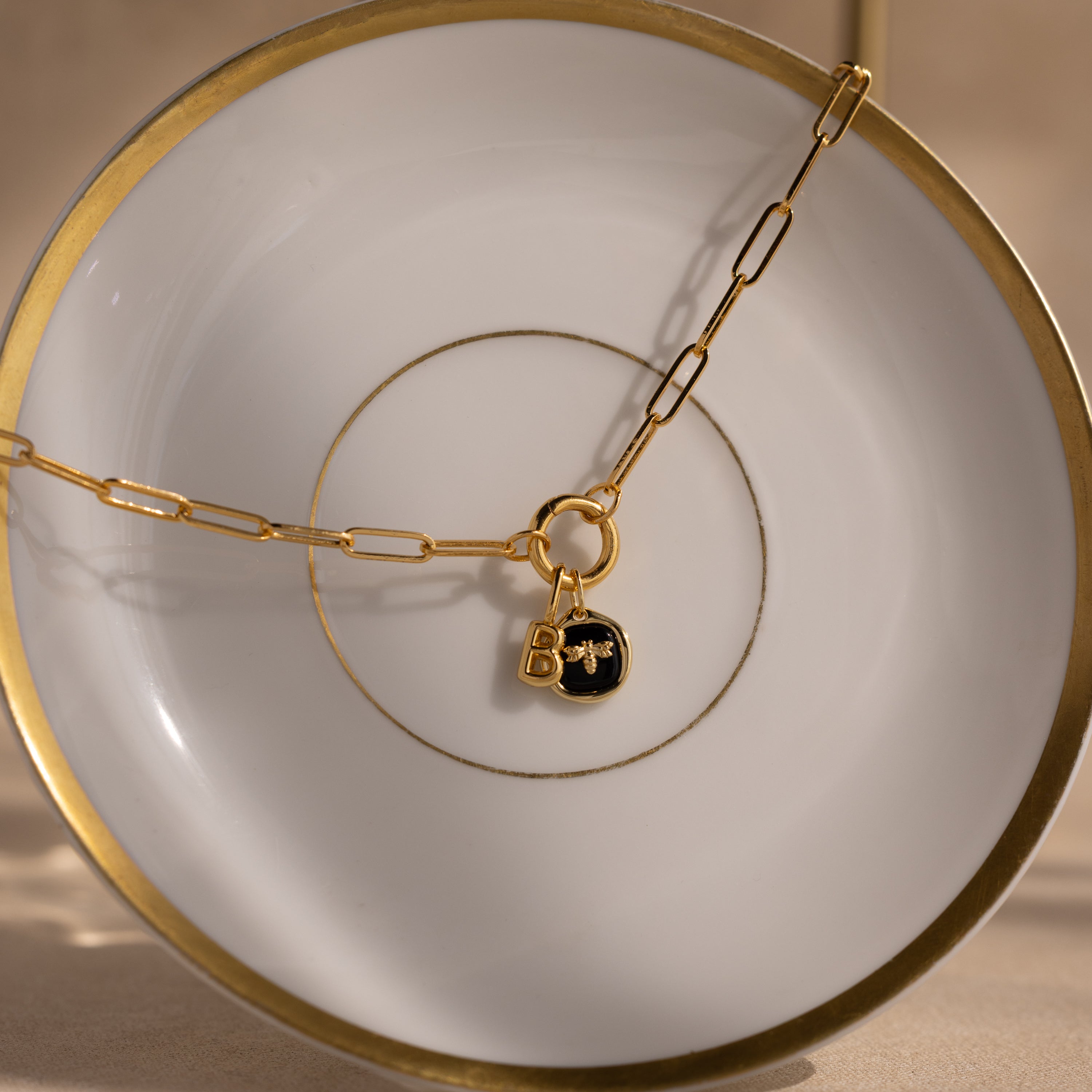 Onyx Honeybee Charm in 18K Gold displayed on an elegant white plate with gold trim—a chic, personalized accessory that makes a perfect gift.