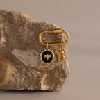 The Onyx Honeybee Charm is a gold keychain featuring a bee and elegant letter B charm, stylishly presented on a beige textured rock for a chic, nature-inspired accessory.