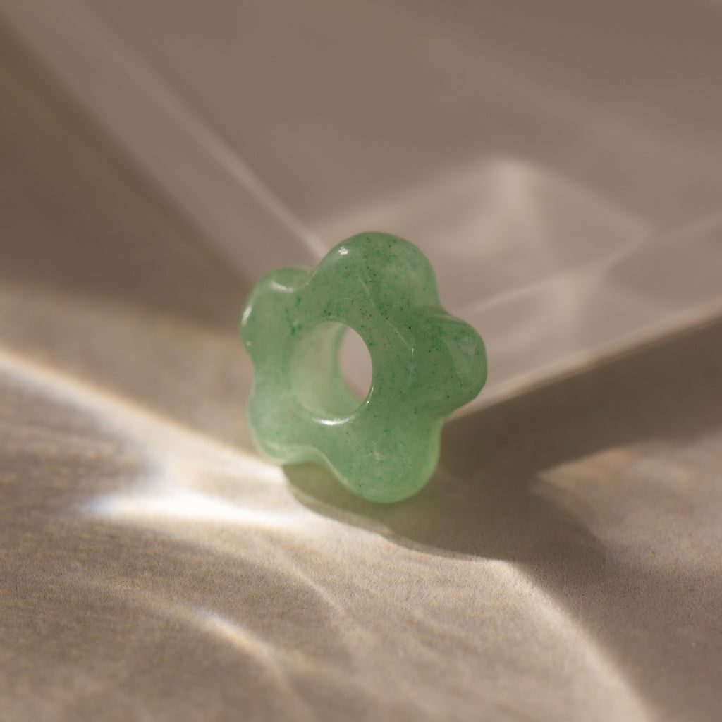 The Jade Flower Charm is a green, flower-shaped stone bead with a central hole, ideal for jewelry making or crafts.