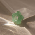 The Jade Flower Charm is a green, flower-shaped stone bead with a central hole, ideal for jewelry making or crafts.
