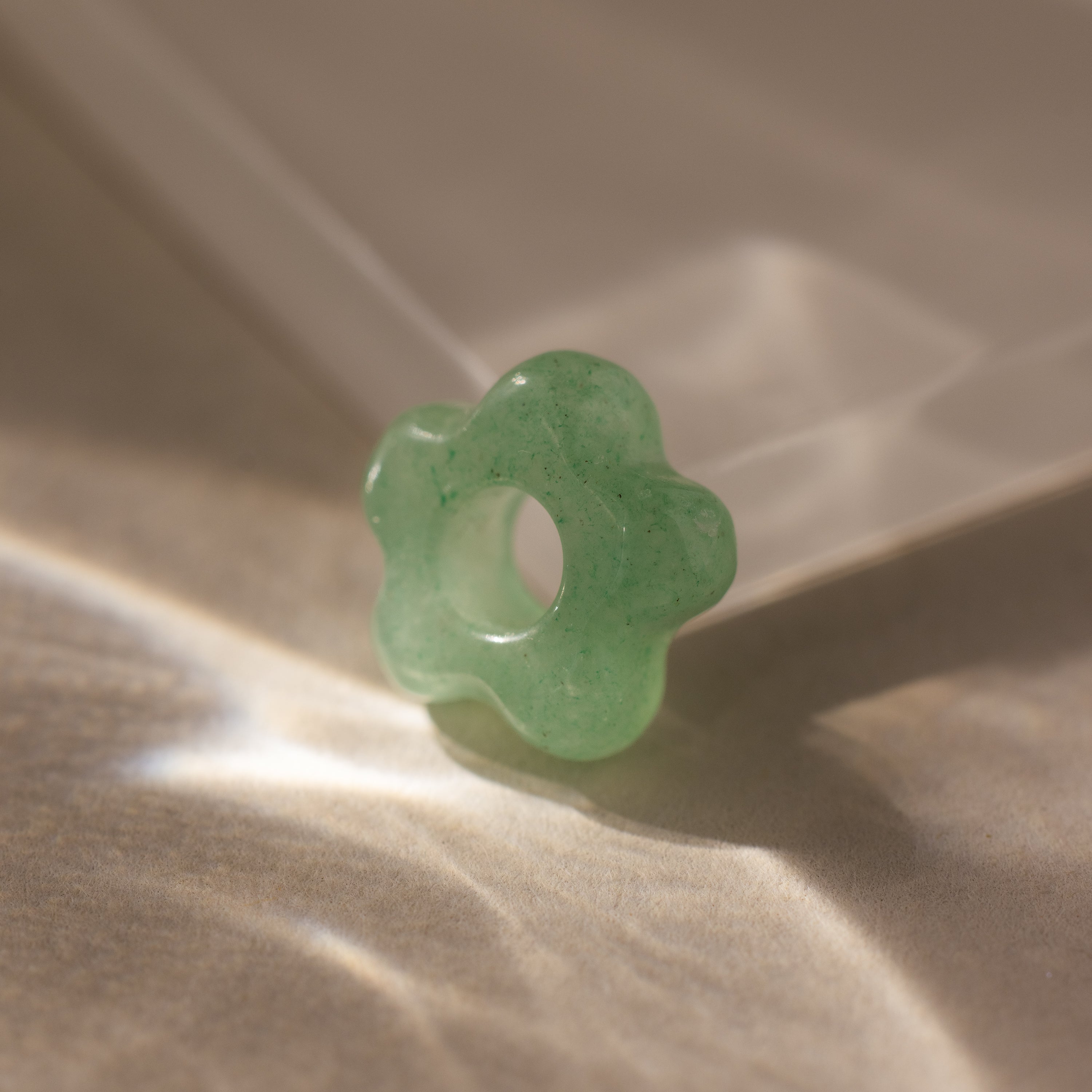 The Jade Flower Charm is a green, flower-shaped stone bead with a central hole, ideal for jewelry making or crafts.