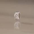 The Sprinkle Diamond Dome Charm in Silver stands upright on a reflective surface, its starburst-set stones and star-shaped engravings shining against a soft beige background.