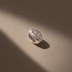 The Sprinkle Diamond Dome Charm in Silver, featuring starburst-set stones and star-shaped engravings, sits illuminated on a beige surface.