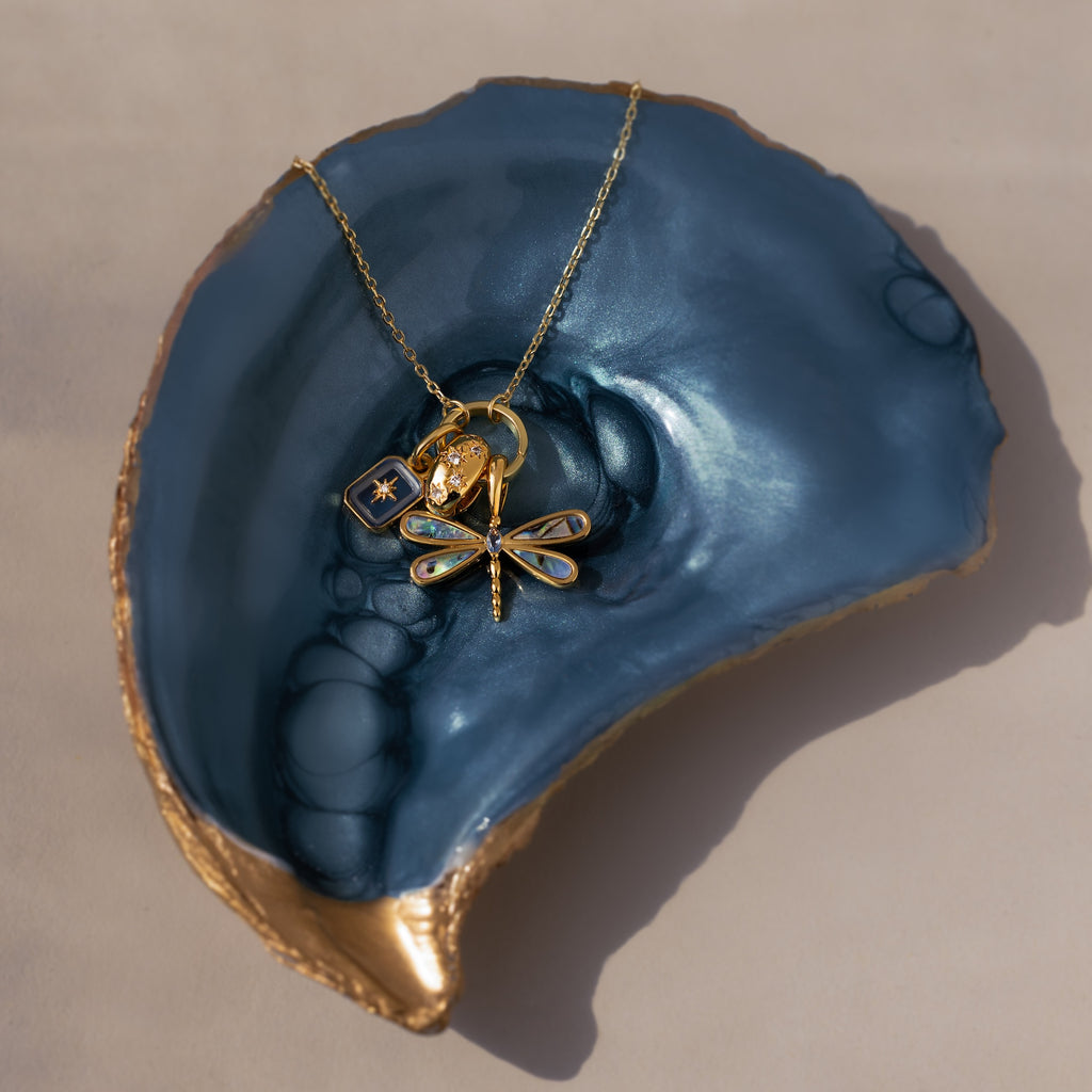 Sprinkle Diamond Dome Charm displayed on a shiny blue and gold shell dish, featuring a stack of charms and starburst-set stones.