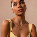 A woman in a yellow top wears two layered gold necklaces, featuring the Sprinkle Diamond Dome Charm, as she gazes slightly upward against a beige background.