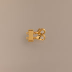 The Double Layering Clasp in 18K Gold features a triple-strand design with two lobster claw closures, ideal for layering necklaces. Displayed on a neutral beige background.