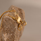 The Double Layering Clasp in 18K Gold, perfect for stacking necklaces, rests on a textured stone with a neutral, blurred background.