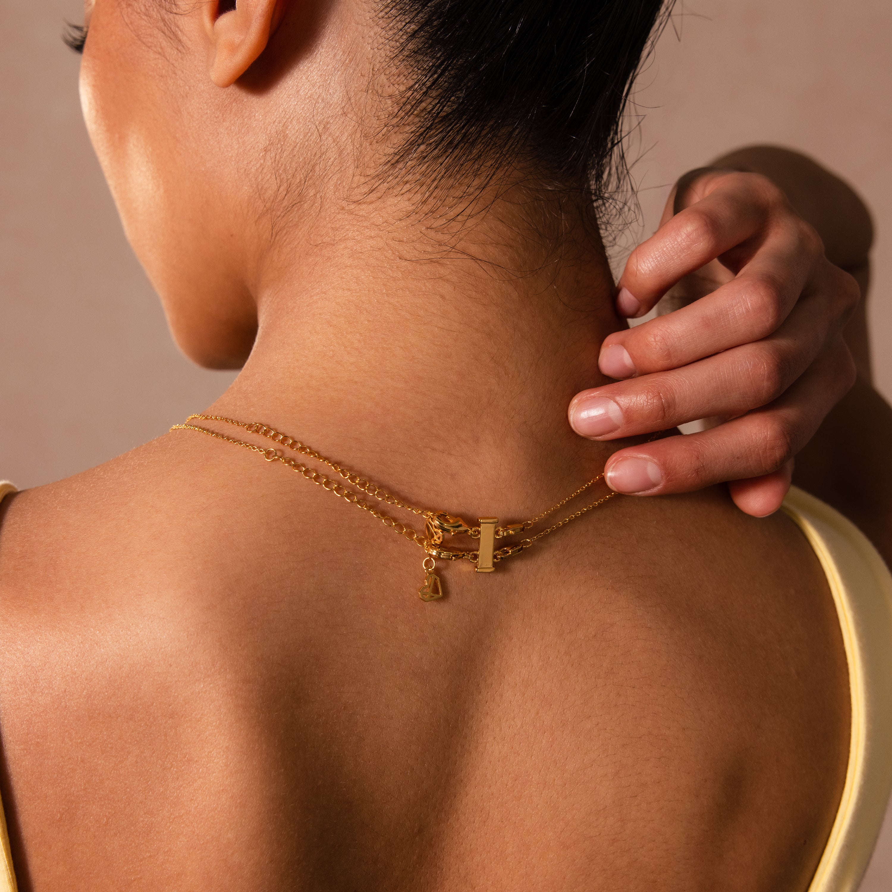 Woman touching her neck, wearing layered silver necklaces with a Double Layering Clasp in Silver and a yellow tank top, seen from behind.