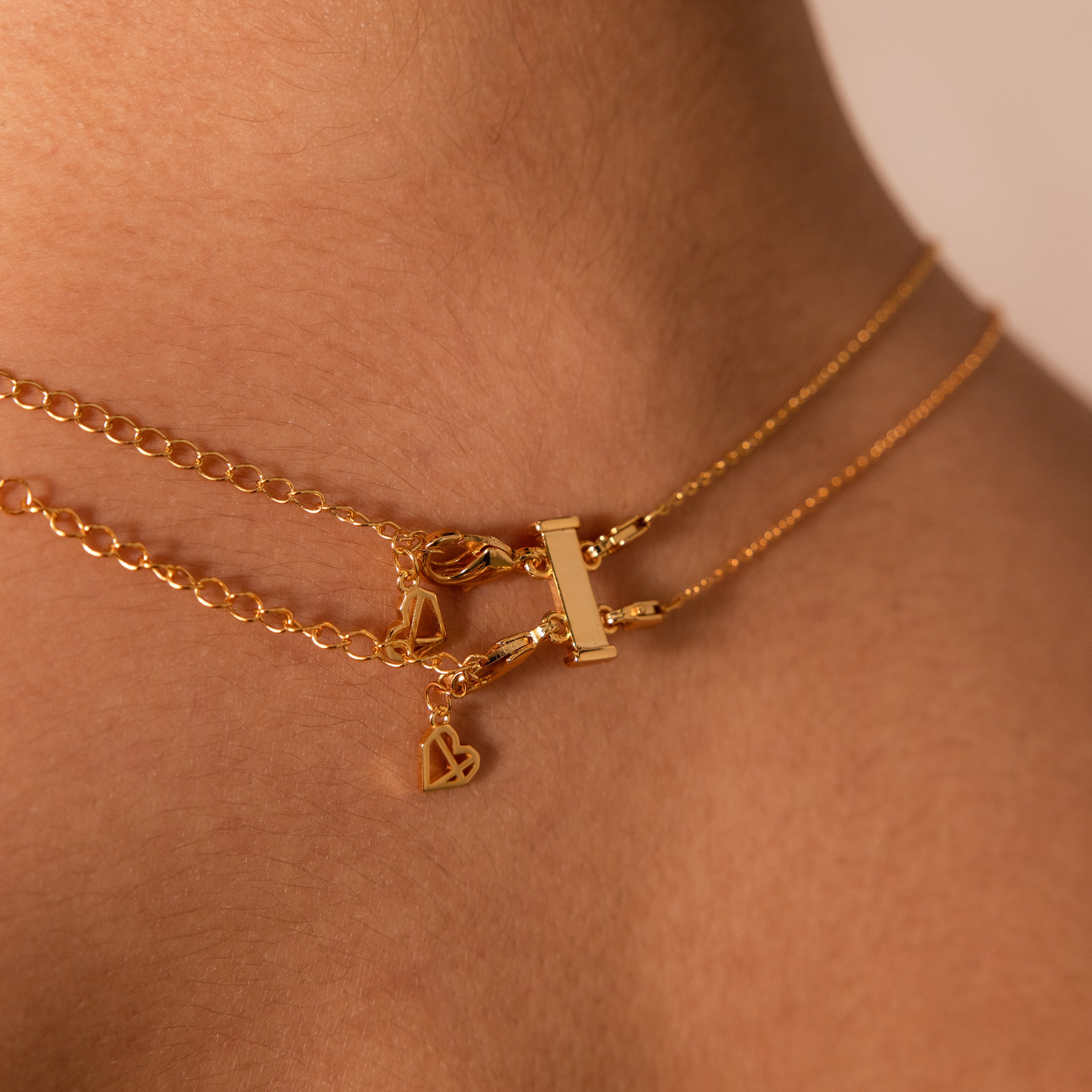 Close-up of a gold necklace with small heart and rectangular charms layered on a neck, featuring stylish stacking using the Double Layering Clasp in Silver for secure dual-lobster-clasp wear.