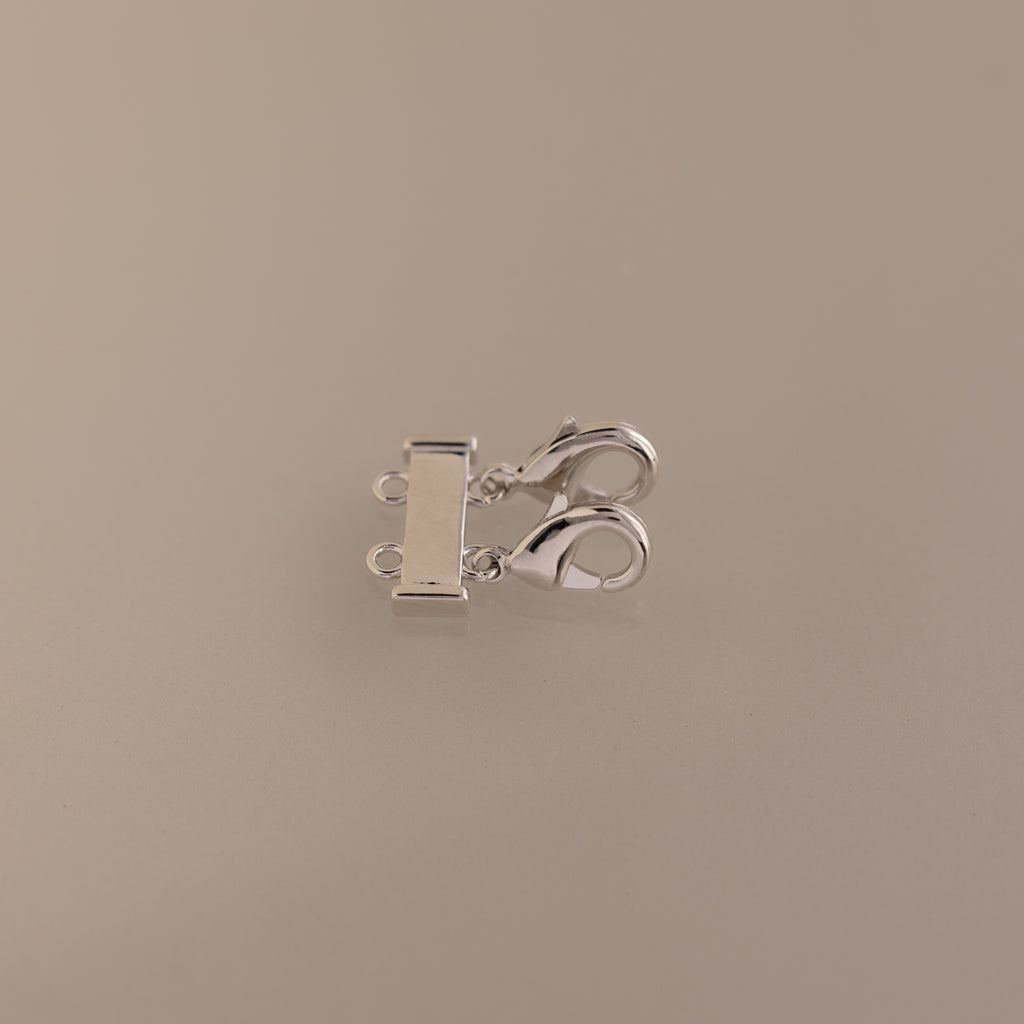 Double Layering Clasp in Silver with dual lobster clasps and three loops for easy necklace layering, displayed on a plain beige background.