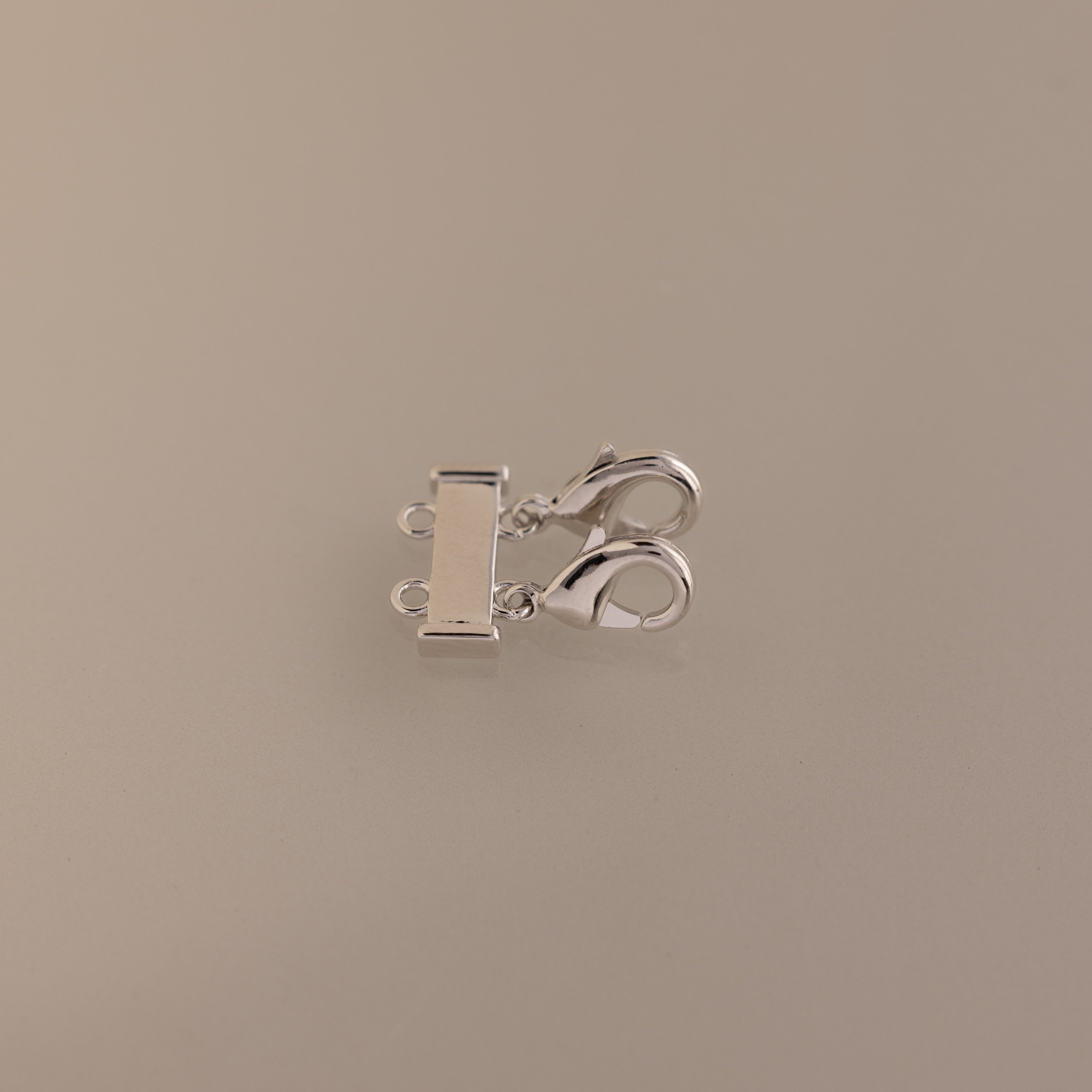 Double Layering Clasp in Silver with dual lobster clasps and three loops for easy necklace layering, displayed on a plain beige background.