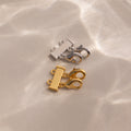 The Double Layering Clasp in 18K Gold, shown here in both silver and gold on a beige surface with soft light reflections, is perfect for effortless necklace layering.
