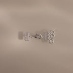 The Triple Layering Clasp in Silver features three loops and a clasp for tangle-free necklace layering, shown on a beige background.