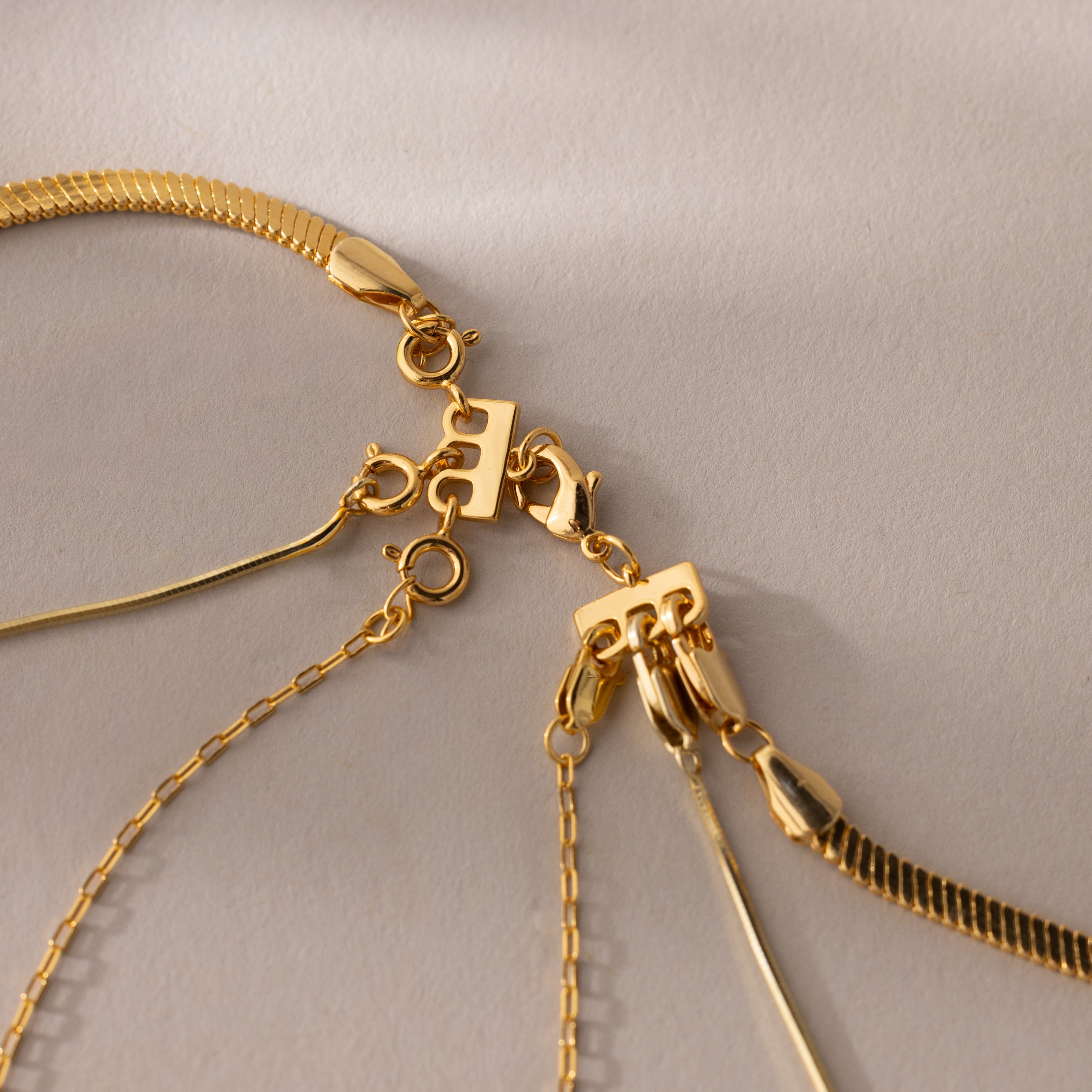 Close-up of three gold necklaces with different chains and clasps on a neutral fabric background—perfect for necklace layering with the Triple Layering Clasp in Silver, which ensures a no-tangle look.