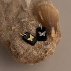 The Onyx Butterfly Charm in Silver features a delicate butterfly design on a sleek black rectangular pendant, combining nature-inspired elegance with modern style.
