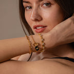 A woman poses with her arm raised near her face, showcasing the elegant Onyx Butterfly Charm in 18K Gold bracelet.