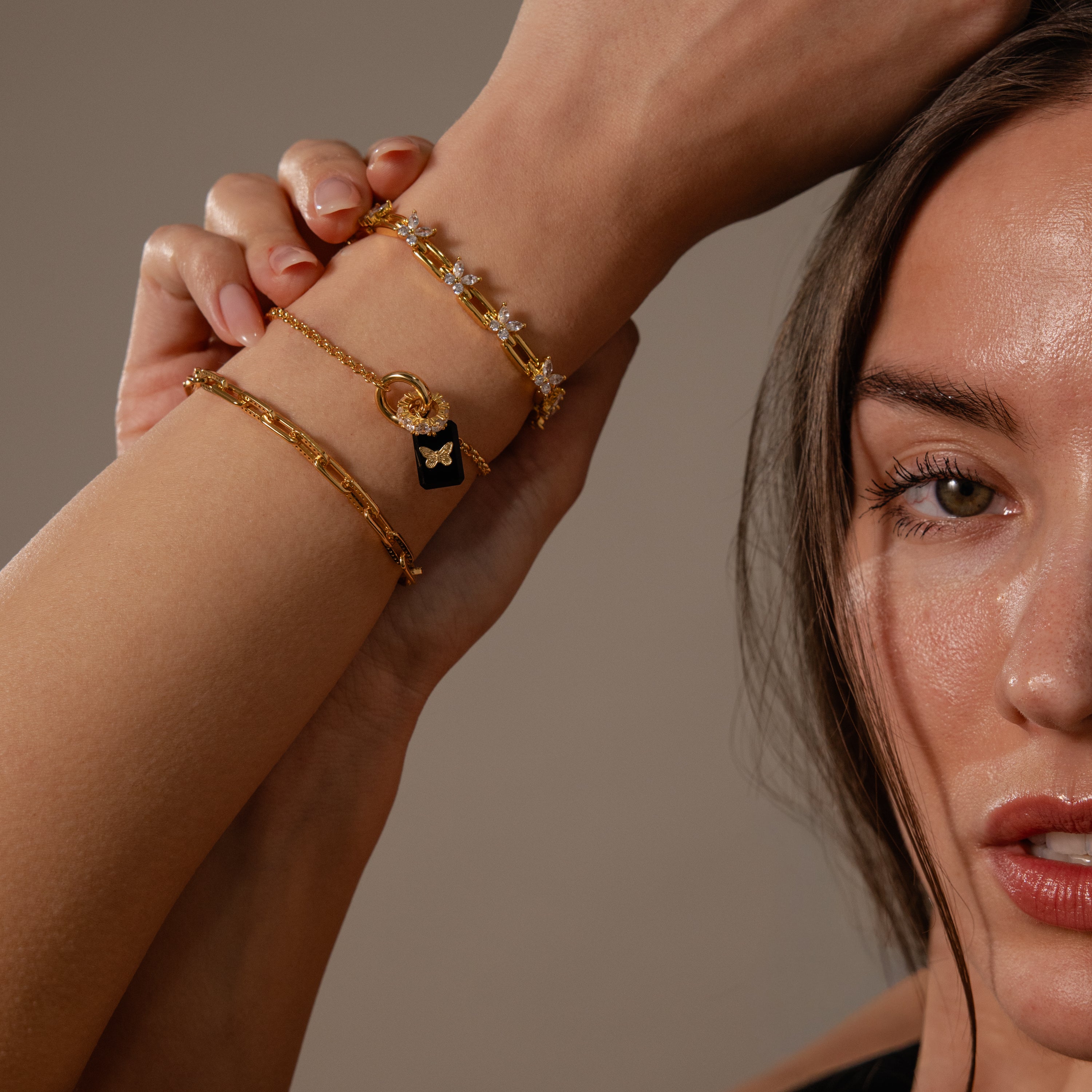 A woman poses with her arm raised, displaying gold bracelets featuring the Onyx Butterfly Charm.