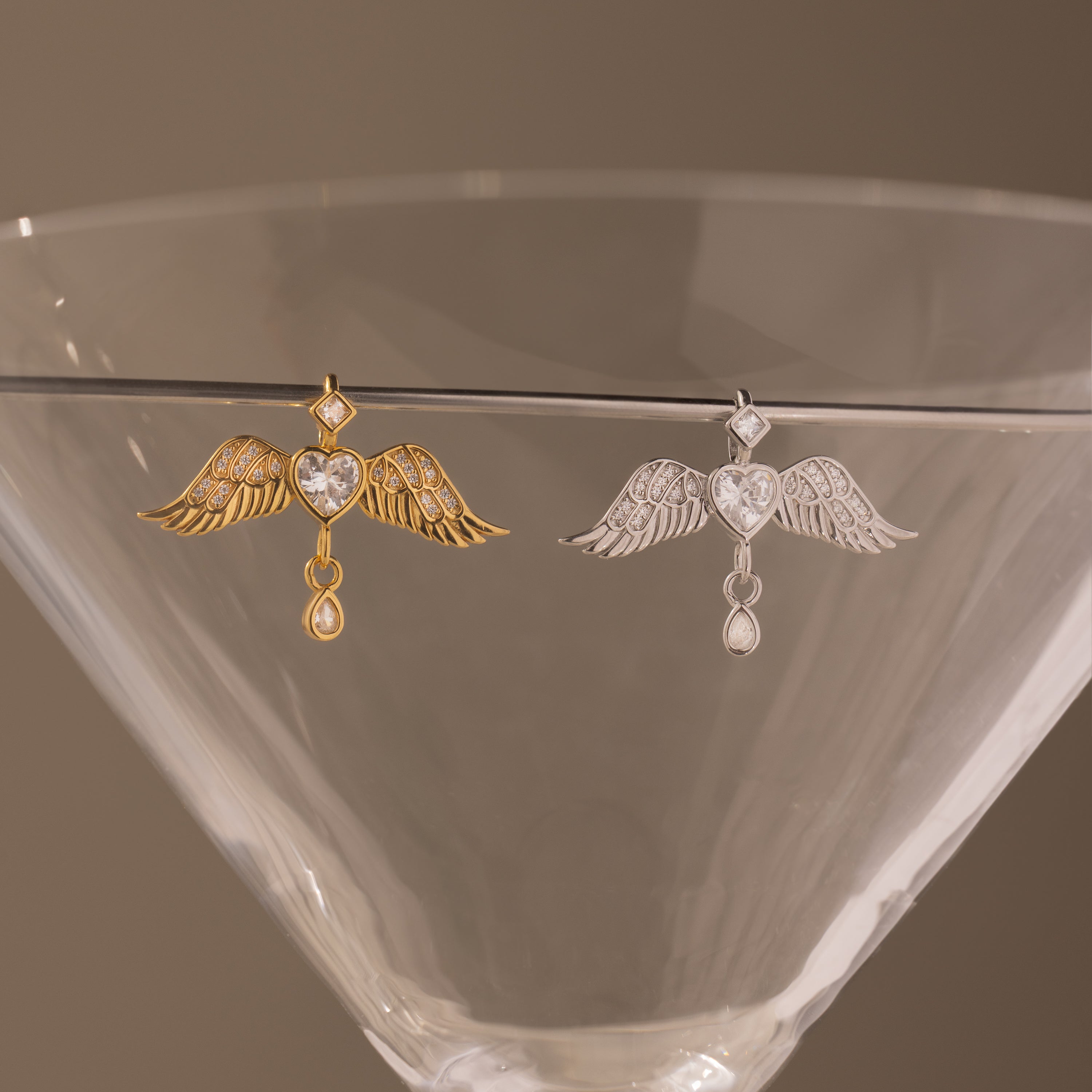 Gold and silver Angel Wing Charms with pavé diamond crystals, draped on a martini glass—ideal as protection jewelry or a sophisticated pendant.