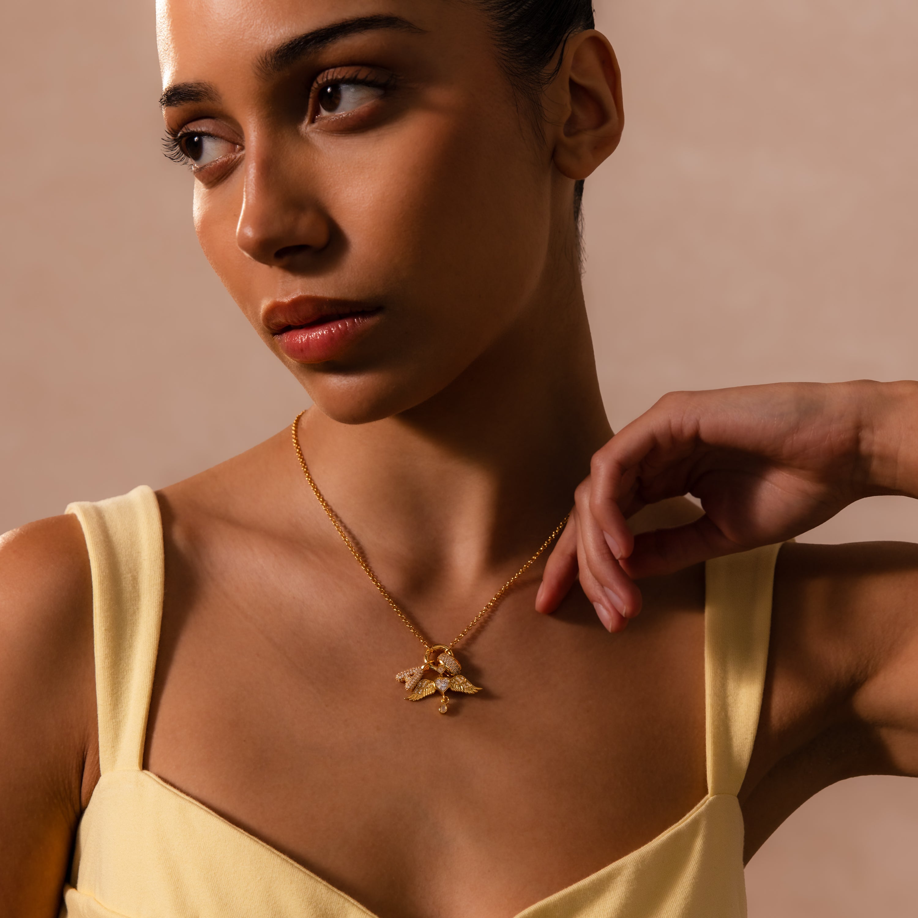 A woman in a yellow top showcases the Bold Pave Dome Charm in 18K Gold, its sparkling pendant adding a touch of elegance and charm to her look against a stylish beige background.