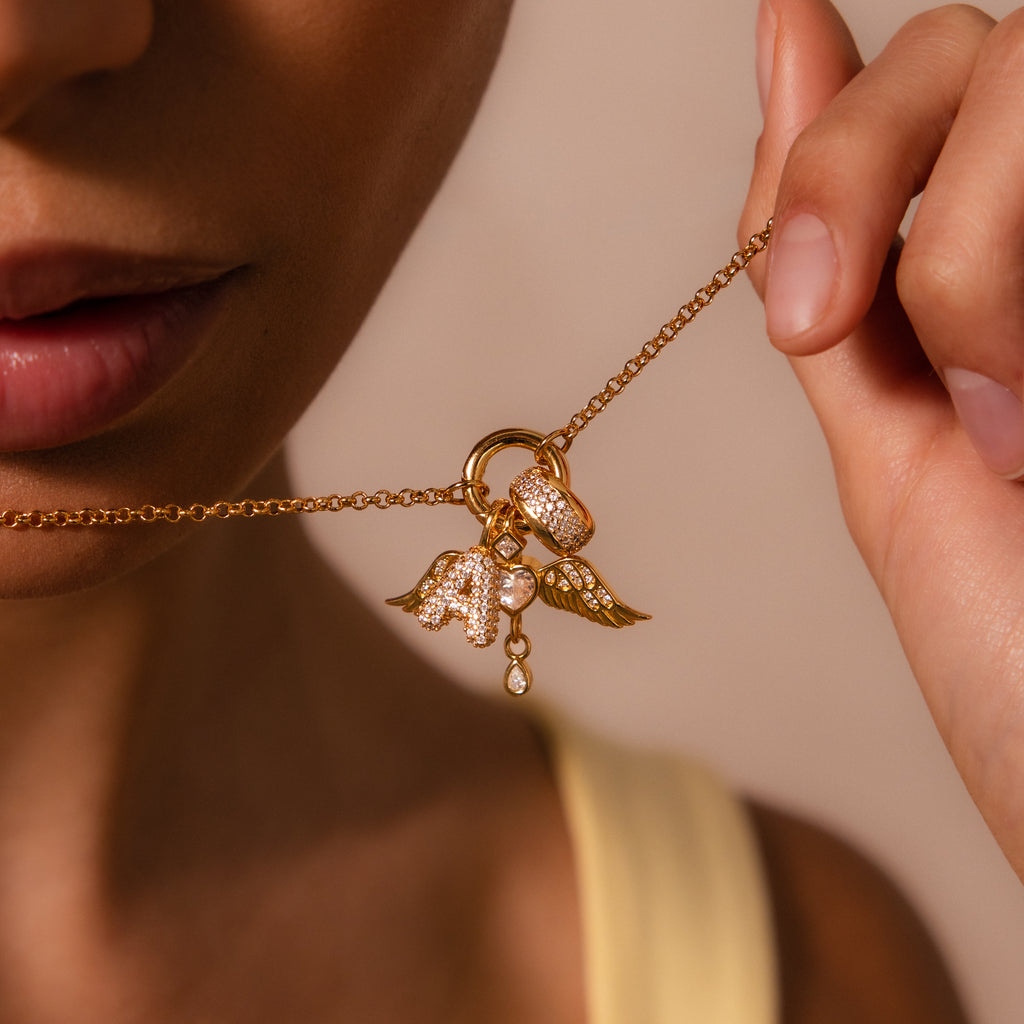 A woman delicately holds the Bold Pave Dome Charm in 18K Gold near her lips, radiating elegance and grace.