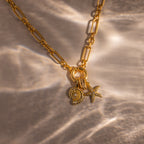 The Pave Dome Charm in 18K Gold adds subtle sparkle with its sun, shell, and starfish-inspired design, perfect for a gold chain necklace on a textured, sunlit surface.
