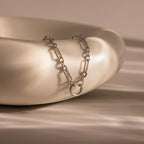Rolo Circle Figaro Necklace in Silver featuring a round pendant and elegant link design, displayed draped over a smooth, cream-colored ceramic bowl.