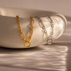 The Rolo Circle Figaro Necklace, a gold and silver chain, is elegantly draped over the edge of a smooth white ceramic bowl.